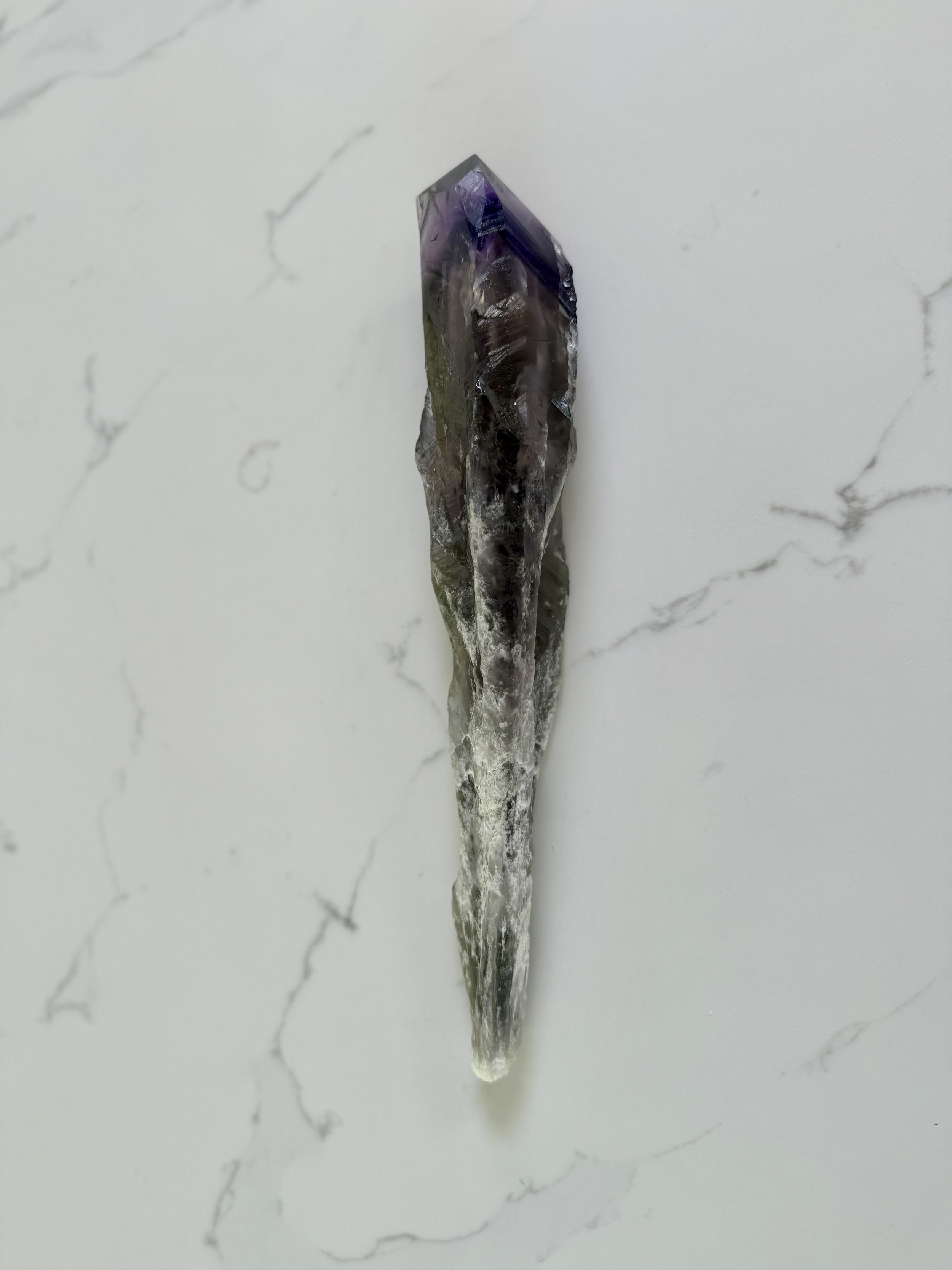 A pointed purple and clear crystal on a pale stone surface.